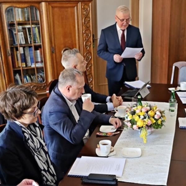 grupa osób siedzący przy stole, prowadzący przemawia na stojąco