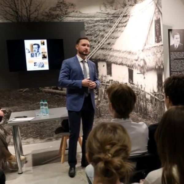 mężczyzna w garniturze stojący na tle ciemnej ściany
