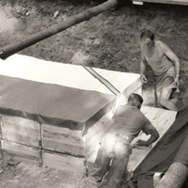 archiwalne zdjęcie, dwóch mężczyzn układa drewniane skrzynie - Złożenie dziewięciu skrzyń ze szczątkami polskich oficerów do grobu, który stanowił pierwotny dół śmierci w Charkowie-Piatichatkach, sierpień 1991 r., fot: Andrzej Świderski 