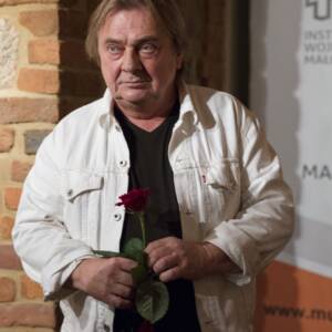 Mężczyzna w czarnym podkoszulku i białej rozpiętej koszuli trzyma czerwoną róże. Autor obrazów Jerzy Martynów