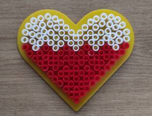 biało czerwone serce. Na żółtym tle w kształcie serca przyklejone cylindryczne koraliki. Tworzą one biało-czerwoną flagę.