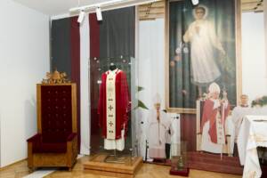 Gablota z czerwonym ornatem oraz fotel z herbem papieskim u góry