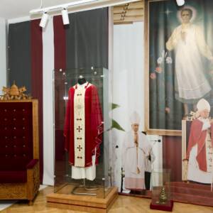 Gablota z czerwonym ornatem oraz fotel z herbem papieskim u góry