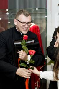 Młody ksiądz przyjmuje czerwoną różę od młodej kobiety.
