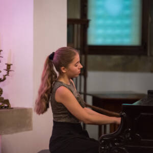 Młoda dziewczyna gra na dużym czarnym fortepianie.