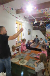 mężczyzna pokazuje dzieciom przy stolikach długi cienki przedmiot.