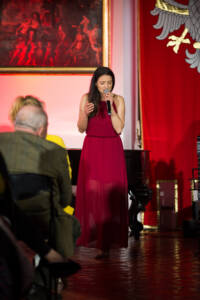 Kobieta w czerwonej sukni śpiewa do mikrofonu.