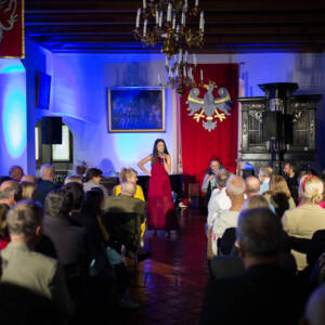 Kobieta w czerwonej sukni śpiewa przed widownią.